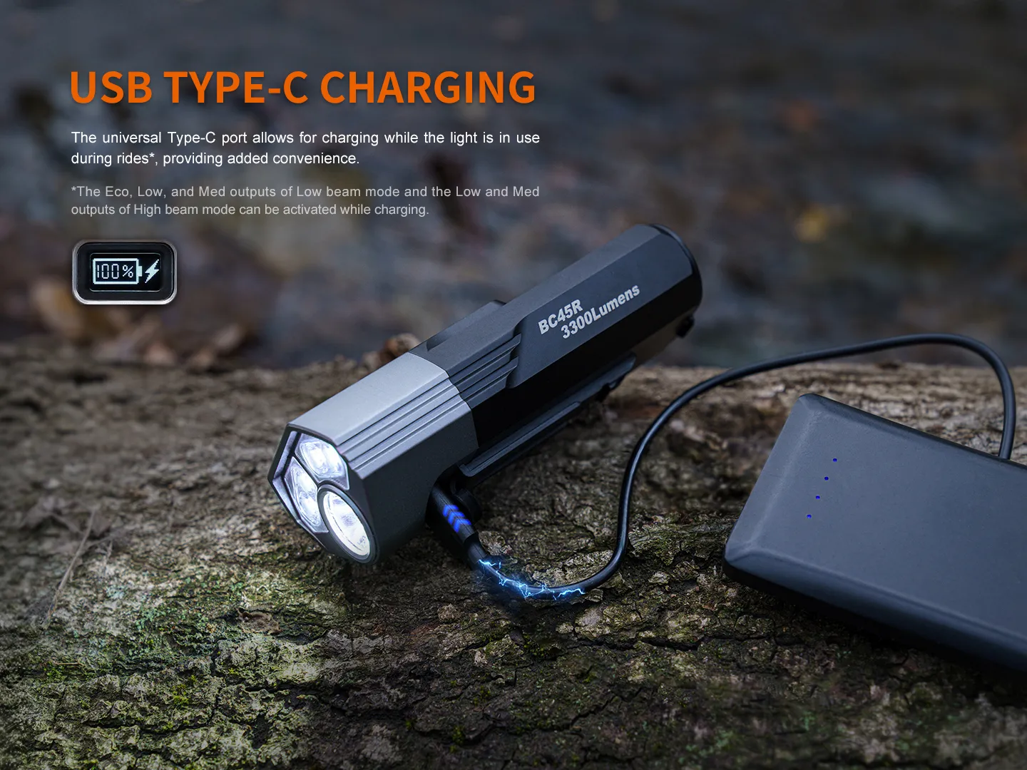 USB Type-C charging setup: battery pack connected to a high-lumen flashlight (BC45R 3300 Lumens) resting on a log outdoors with a power bank nearby. It highlights charging capability and outdoor use.
