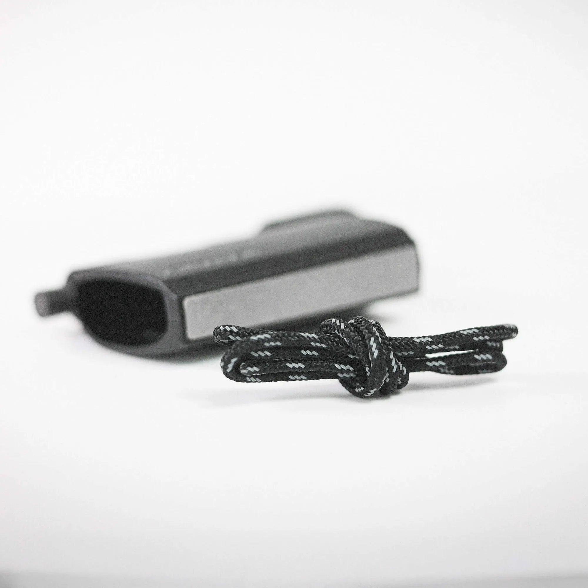 Close-up of a black handgun on a light surface with a braided black cord laying in front of it.